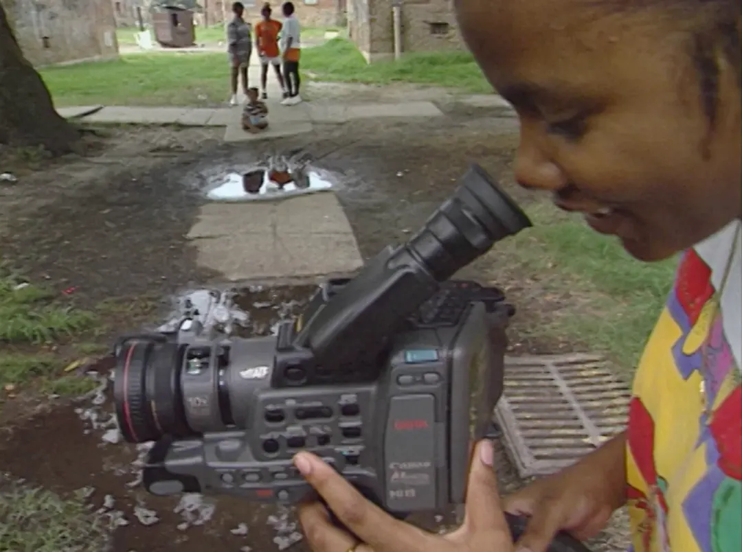 Black boy looks into an old video camcorder in profile view.