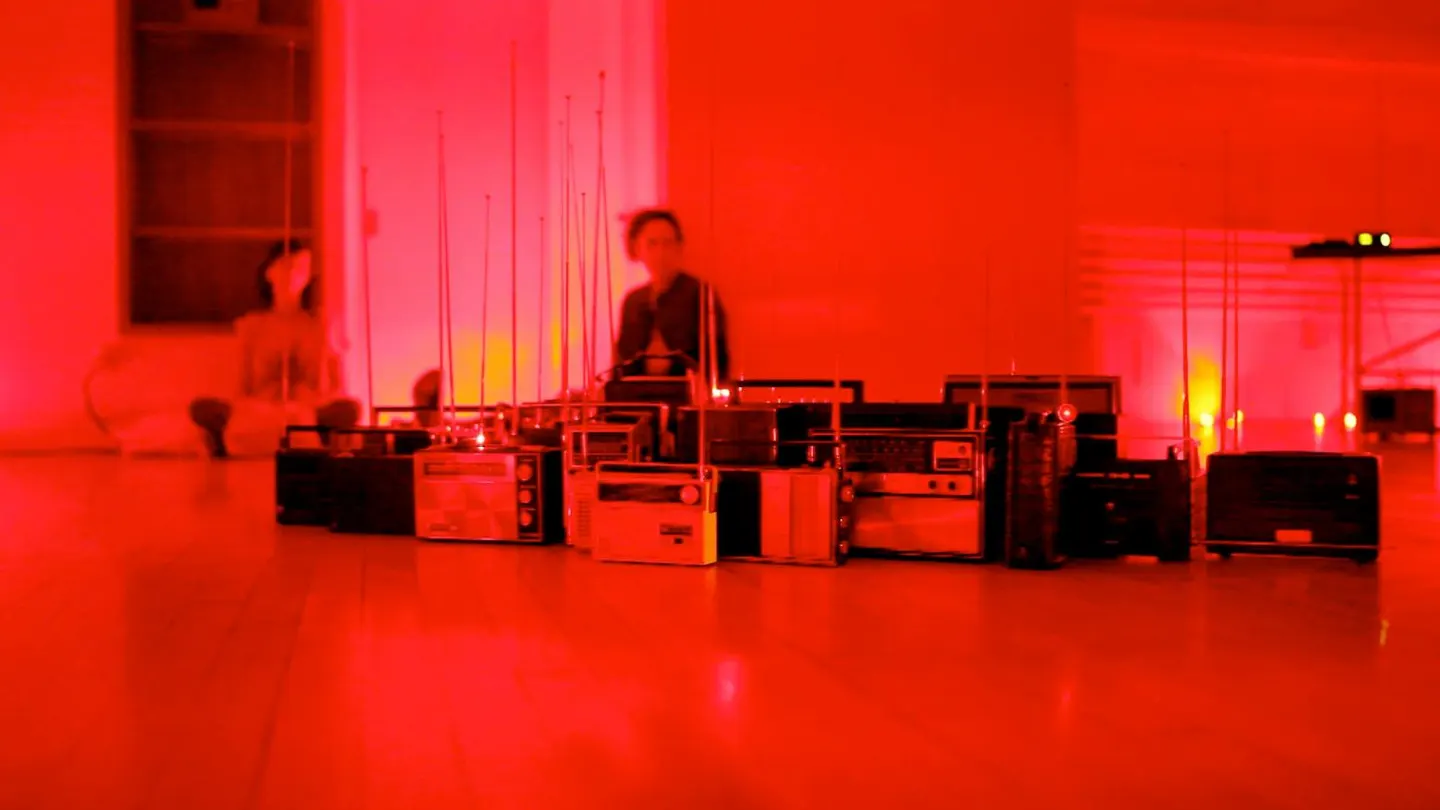 Photo of the Anna Friz performing with multiple radios on the floor under a red light.