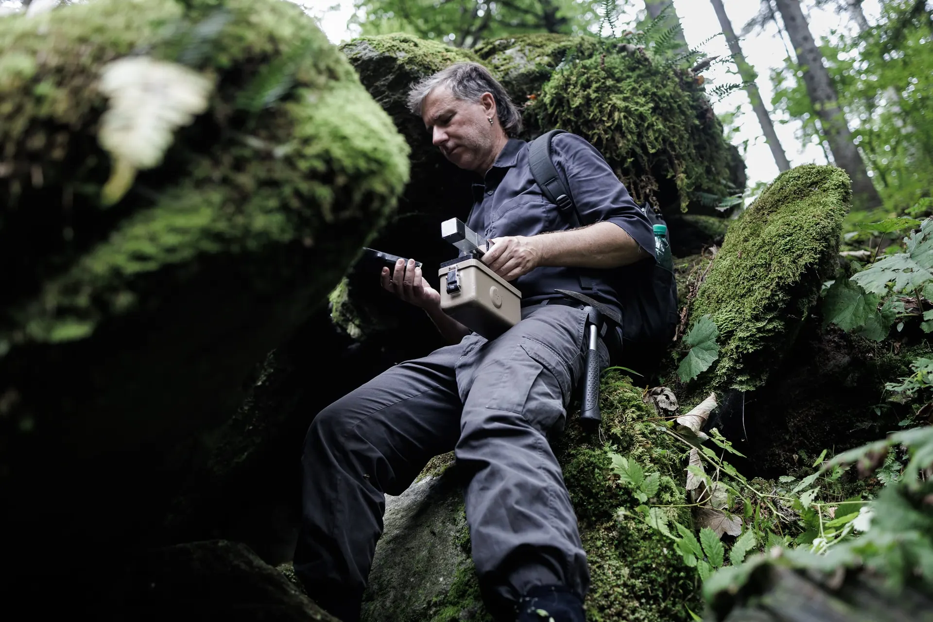 Photo of a Erich Berger with geiger counter next to rocks.