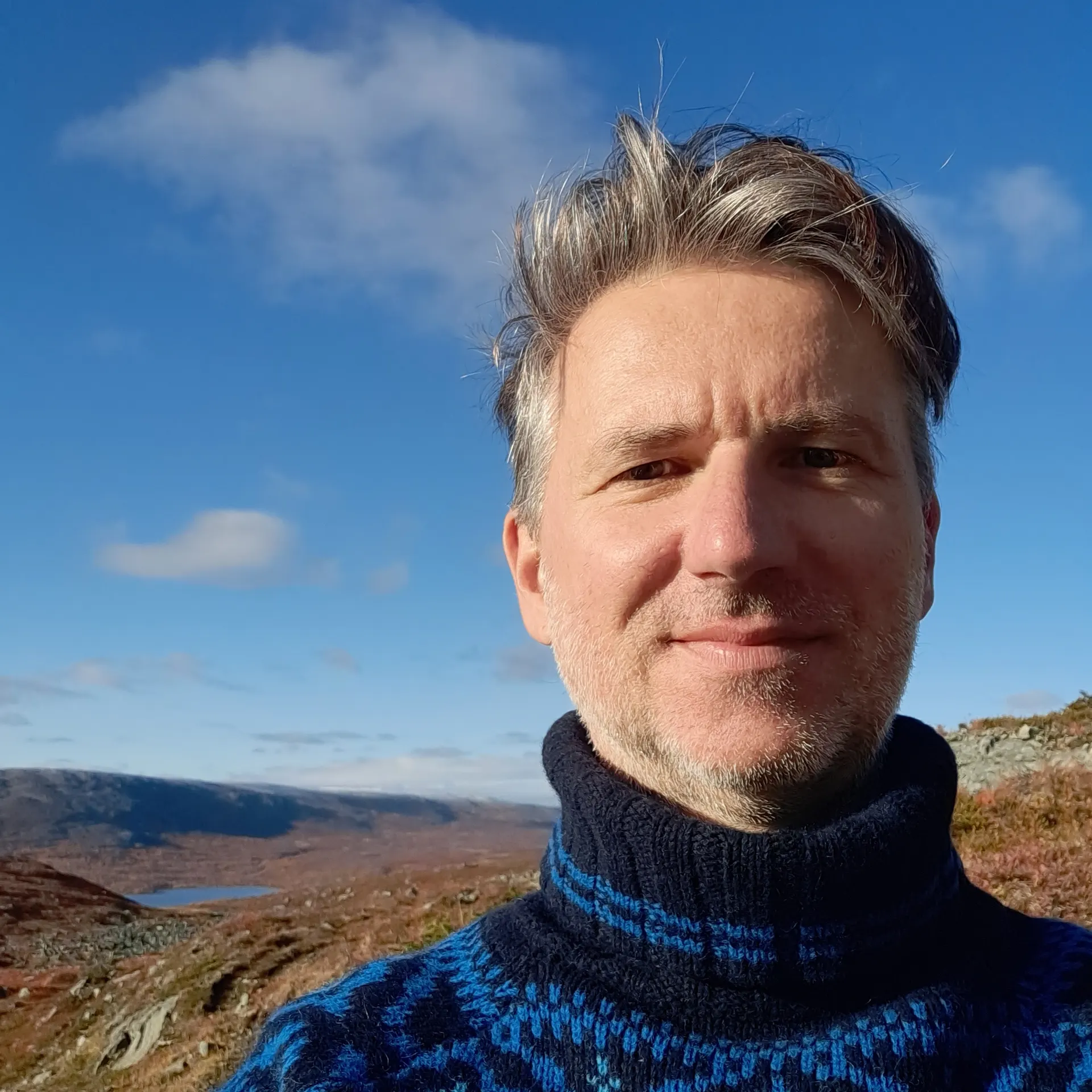 photo portrait of Erich Berger, a middle aged white man with light skin and short hair smiling in an alpine landscape.