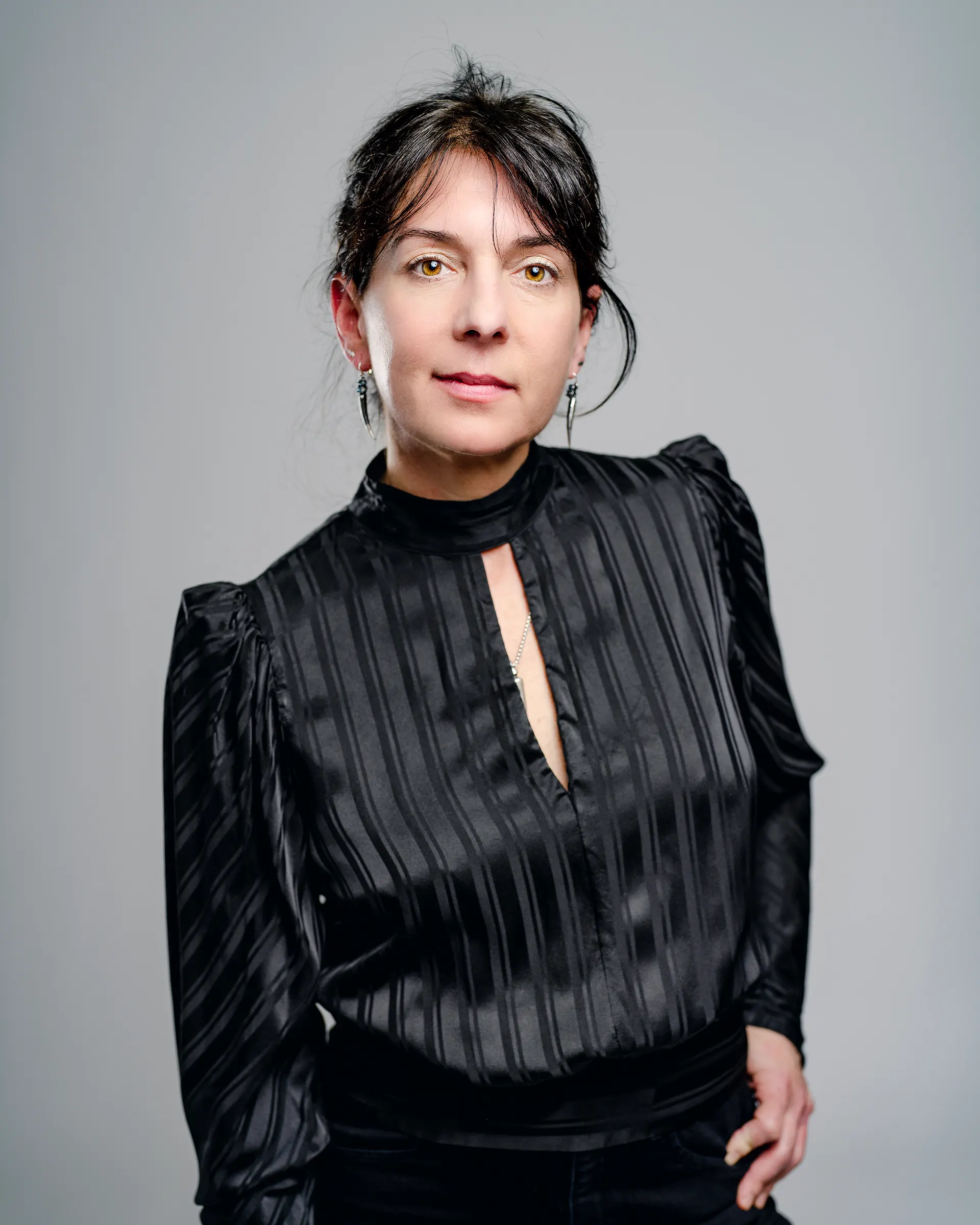 Photo portrait of Galen, a white woman with dark hair and eyes, in an elegant black dress with puffed shoulders. She is looking straight at the camera with a soft smile and dangling earrings.