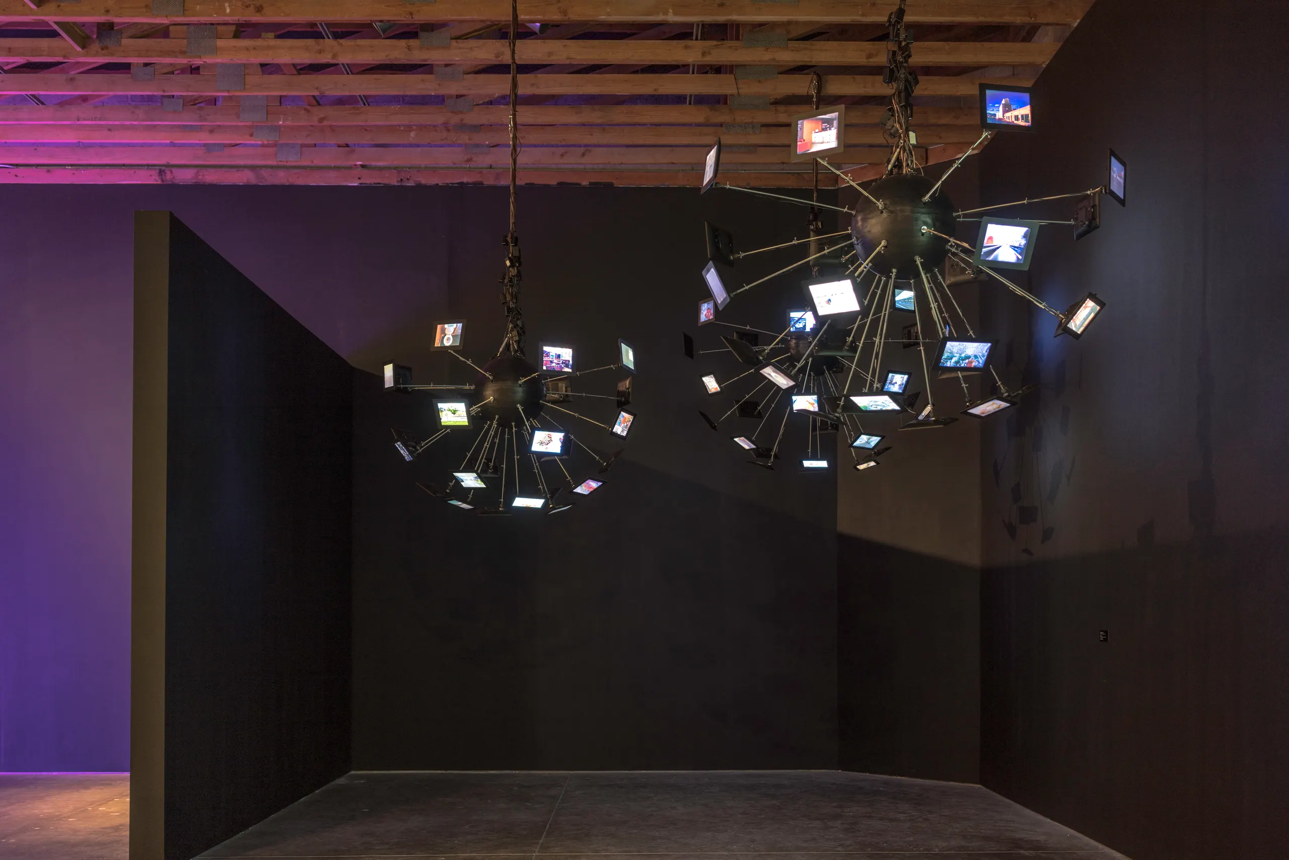 Picture of video installation against a black backdrop with small lcd screens arranged from a central based and hanging from the ceiling like chandeliers.