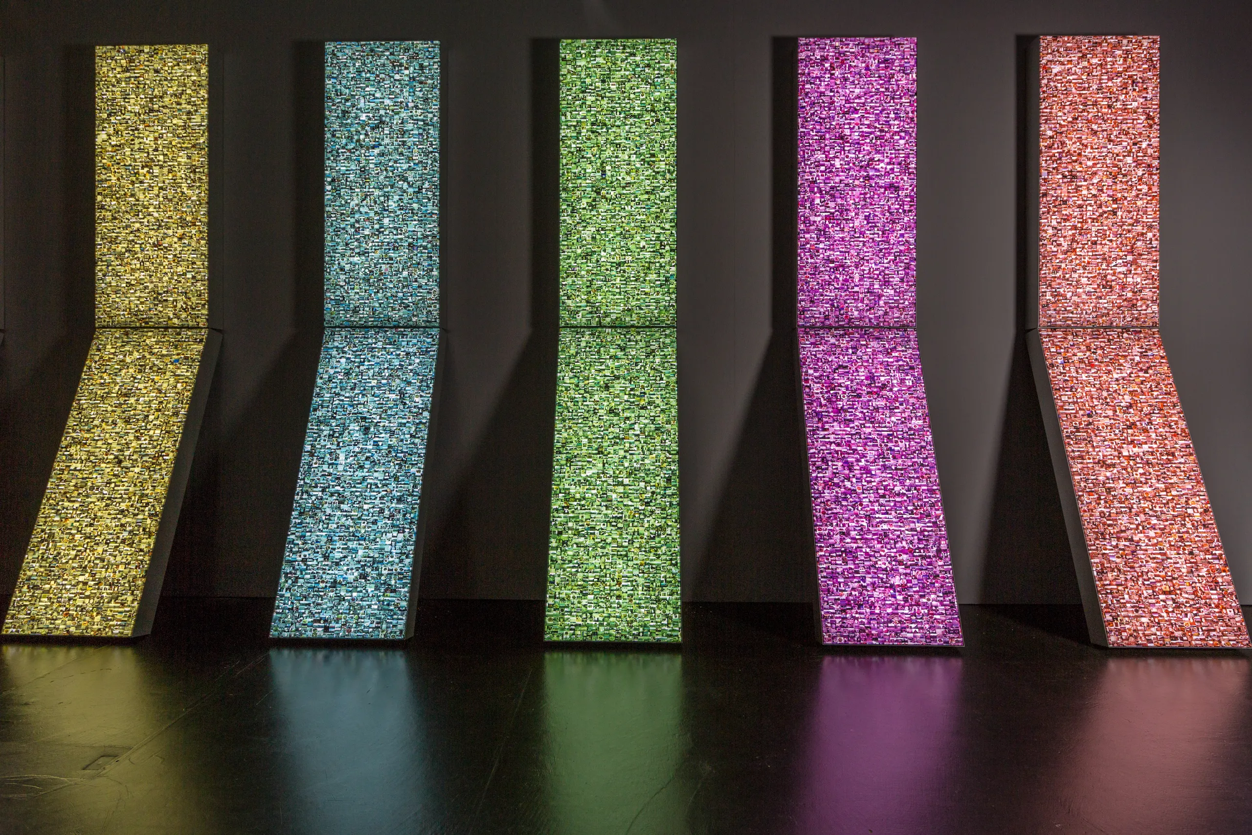 Picture of video installation with 5 V-shaped lcd screens leaning agains the wals, each of different color and composed of smaller images.
