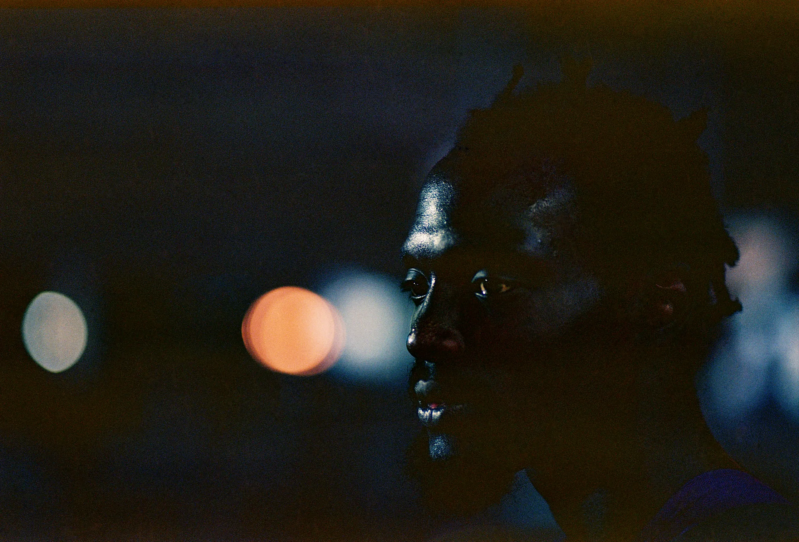 Close up photo of black man in dark surroundings, looking to the right out of view.