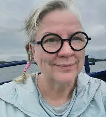 photo portrait of Laura Beloff, a middle aged white woman with light skin and hair, smiling radiantly with dark black glasses.
