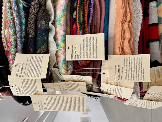 A stack of colorful blankets, each with a paper tag attached.
